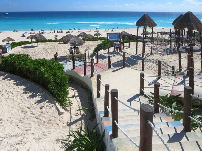 Turistas en Playa Delfines, Cancun, con palapas y el mar del Caribe al fondo