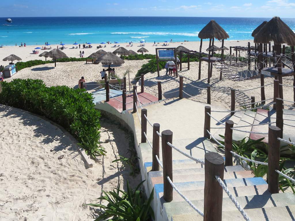 Turistas en Playa Delfines, Cancun, con palapas y el mar del Caribe al fondo